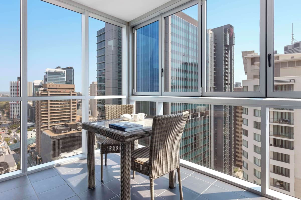Ein Balkon mit Tisch und Stühlen und Blick auf die Stadt durch große Fenster.