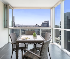 A balcony with a table and chairs, offering a city view.