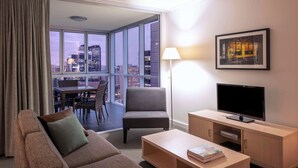 Habitación de hotel moderna con balcón, sofá, sillón, televisor y lámpara.