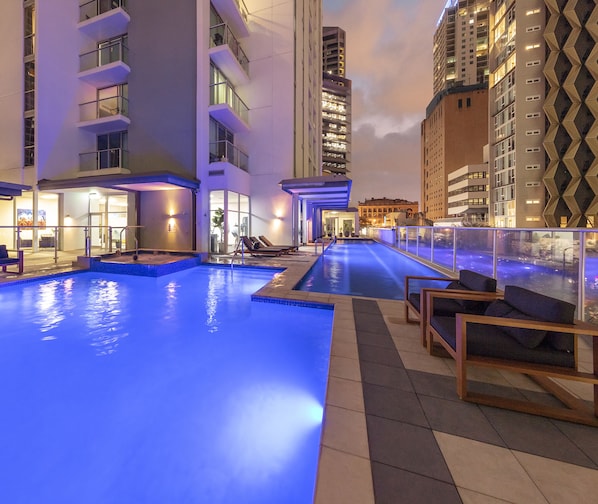 A rooftop pool with lounge chairs and a view of surrounding buildings.