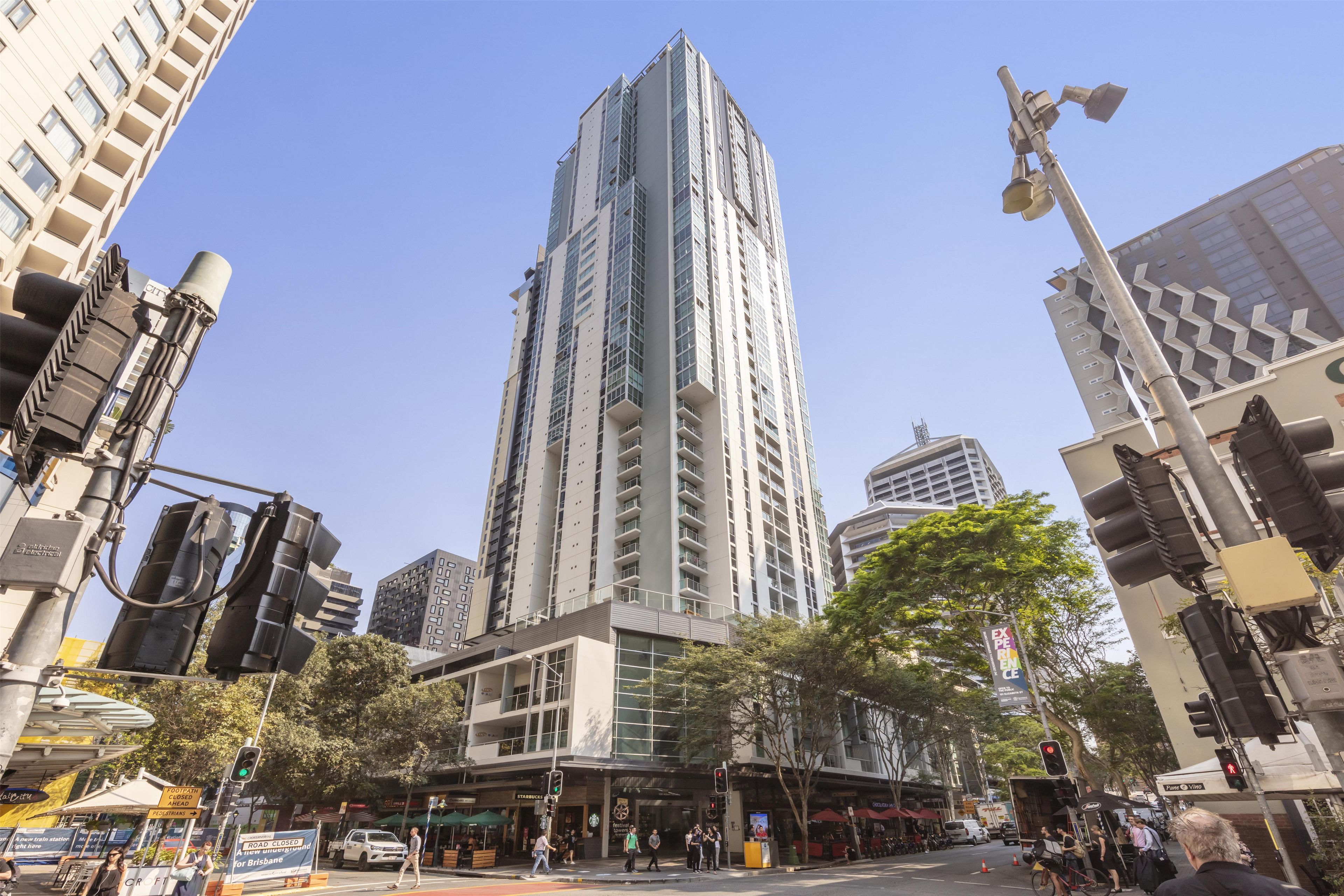 Un edificio de gran altura con varios pisos, rodeado de otros edificios, y una calle con peatones y vehículos.