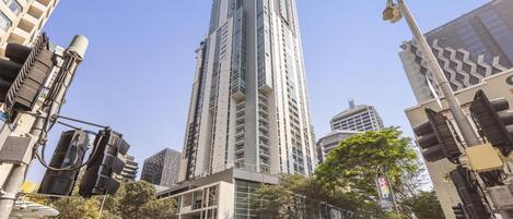Un edificio de gran altura con varios pisos, rodeado de otros edificios, y una calle con peatones y vehículos.