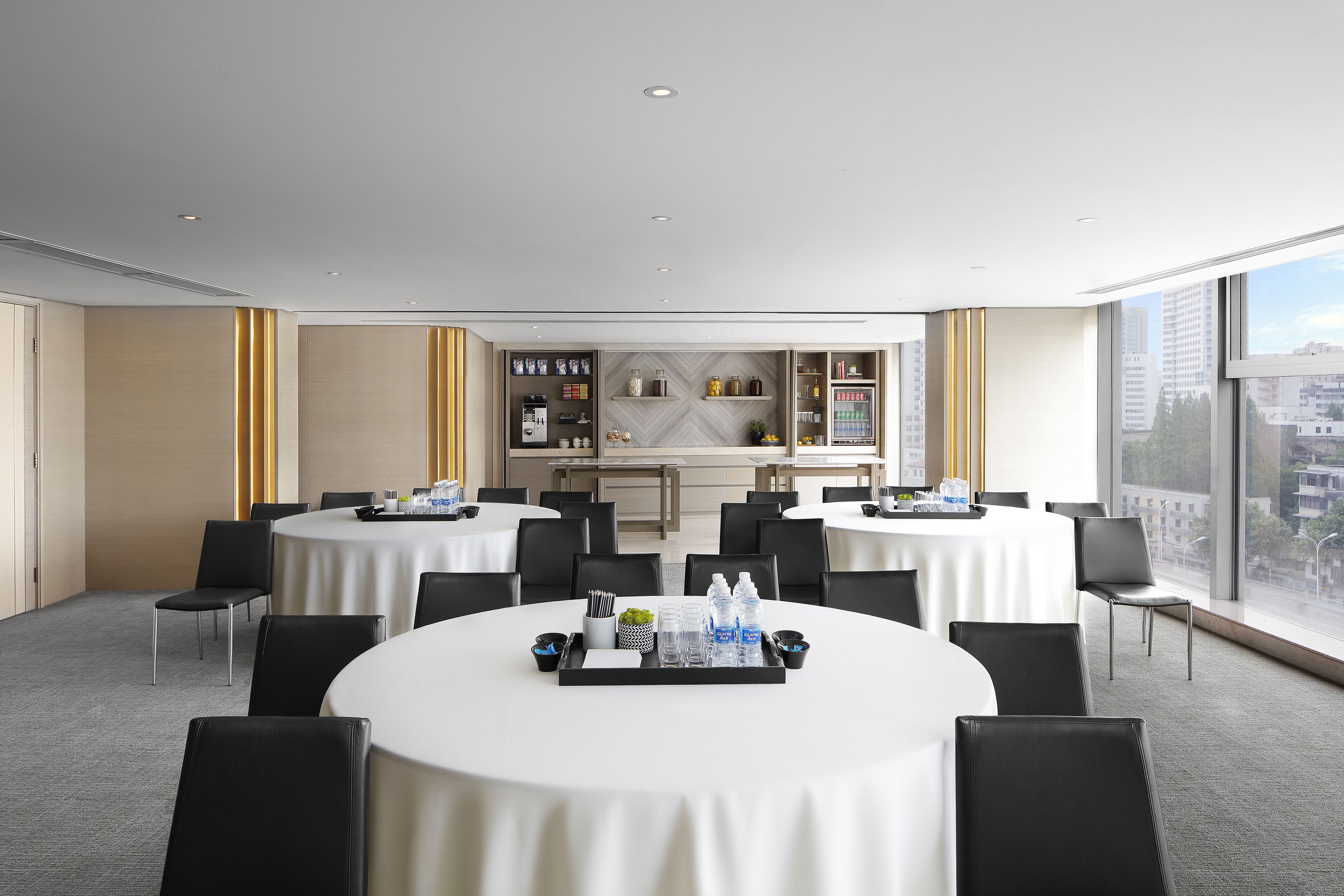 Een moderne congreszaal met ronde tafels, zwarte stoelen en een buffetgedeelte met diverse eten en drinken.