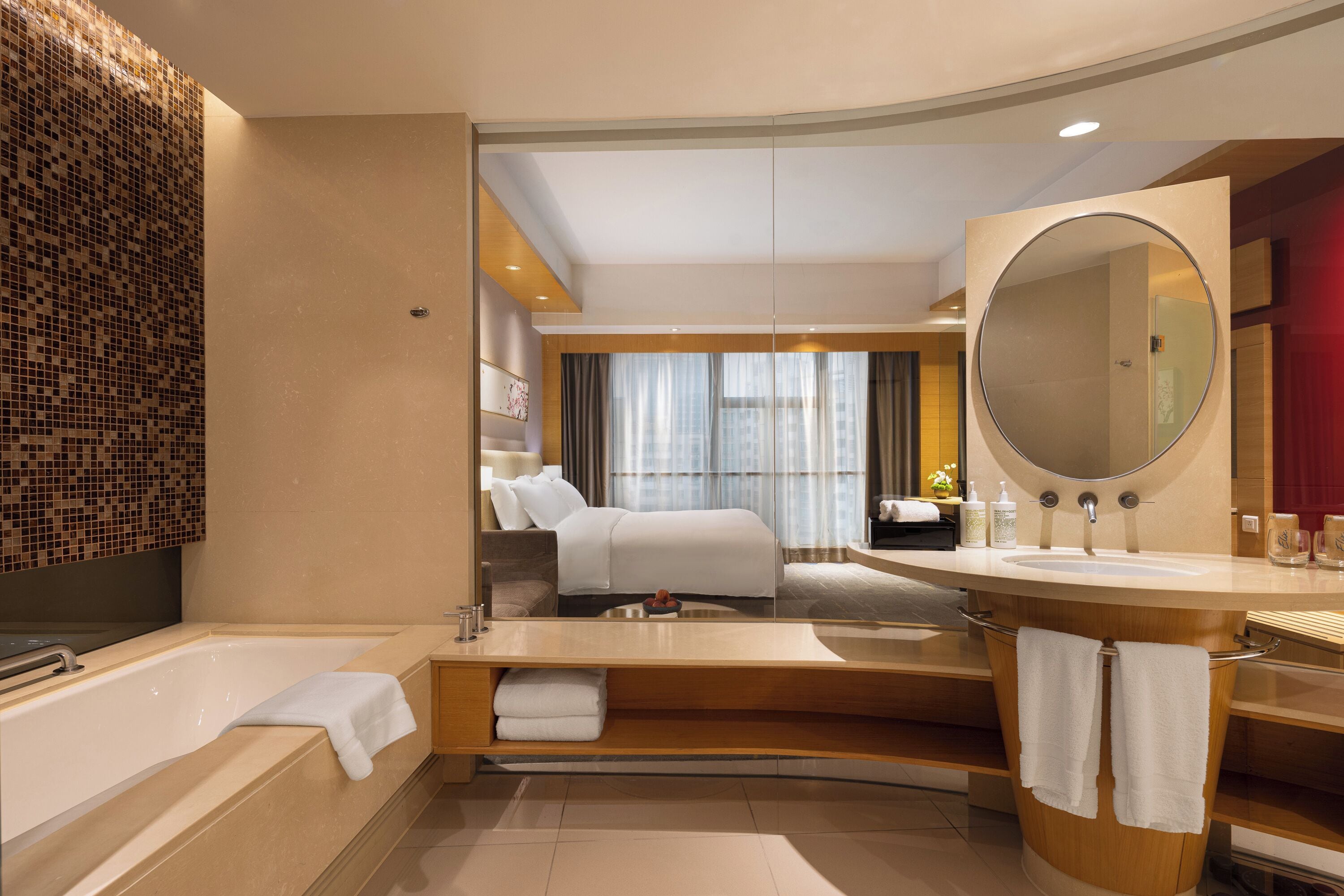 A modern hotel bathroom with a large bathtub, a round mirror, and a separate shower area.