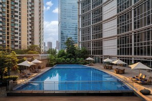 A rooftop pool with lounge chairs and umbrellas, surrounded by high-rise buildings. - New World Wuhan Hotel (Wuhan)