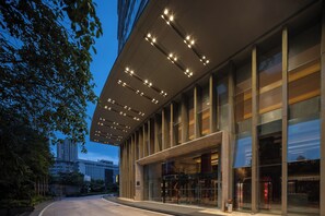 A modern building with a glass facade, large windows, and a covered entrance area with lights. - New World Wuhan Hotel (Wuhan)