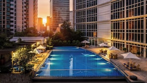 Ein Pool auf dem Dach mit Liegestühlen und Sonnenschirmen, umgeben von Hochhäusern und Grünflächen.