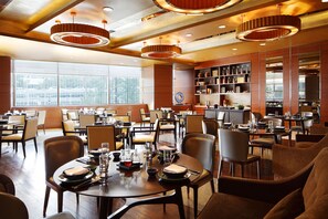 A spacious dining area with multiple tables and chairs, large windows, and modern lighting fixtures. - New World Wuhan Hotel (Wuhan)