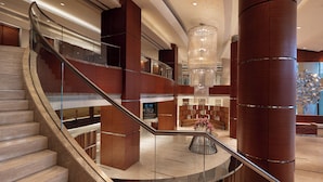 Eine großzügige Lobby mit einer geschwungenen Treppe, einem großen Kronleuchter und einer Sitzecke mit Blick auf die Stadt.