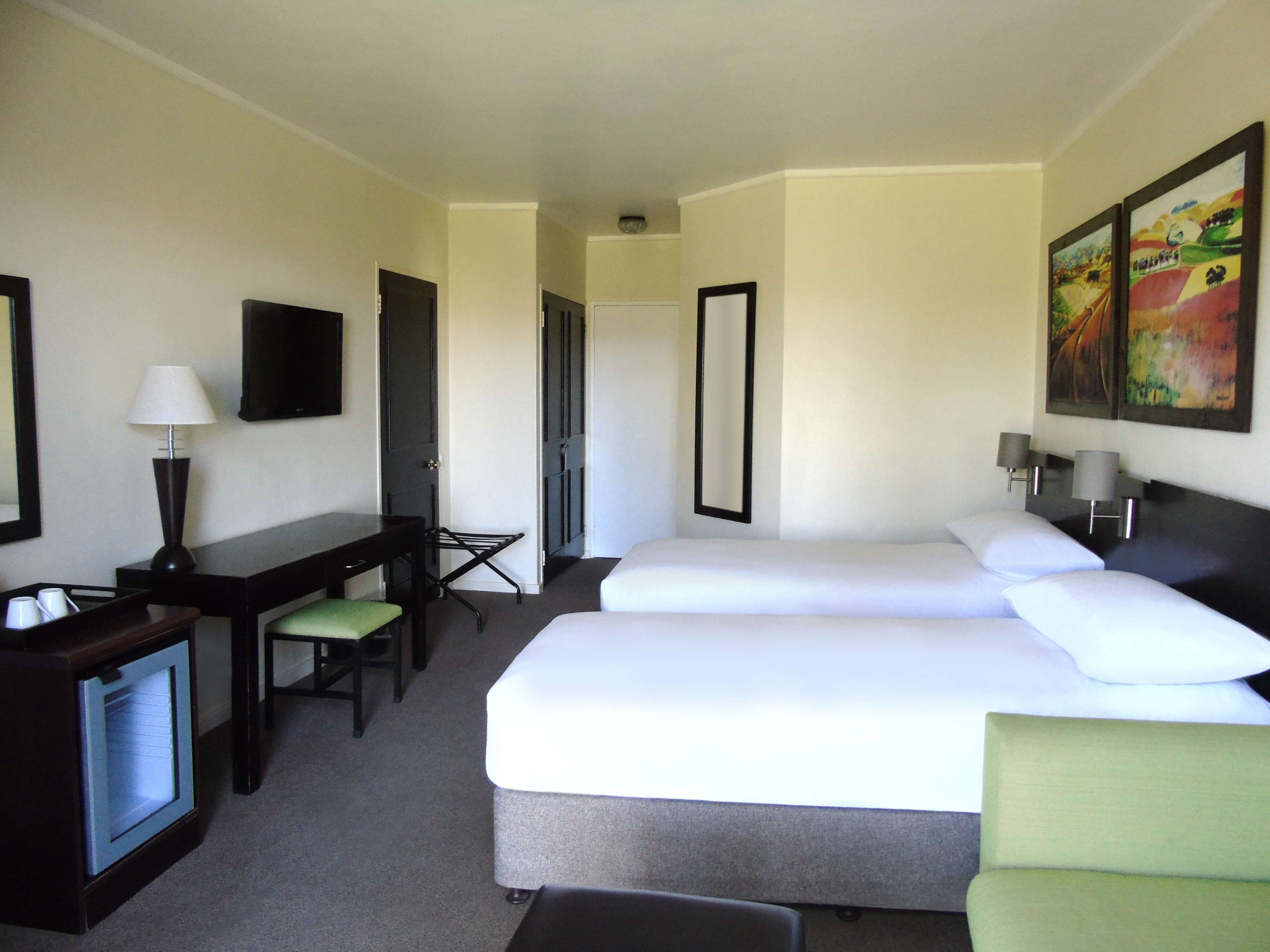 Habitación de hotel con cama, escritorio, silla, televisor y un cuadro en la pared.