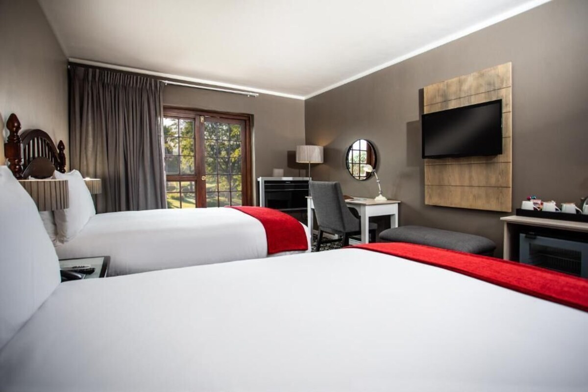 Une chambre d’hôtel avec deux lits, un bureau, une télévision et une fenêtre avec des rideaux.