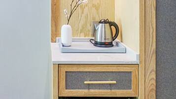 A compact kitchenette with a stainless steel kettle, a small vase with flowers, and a trash bin.