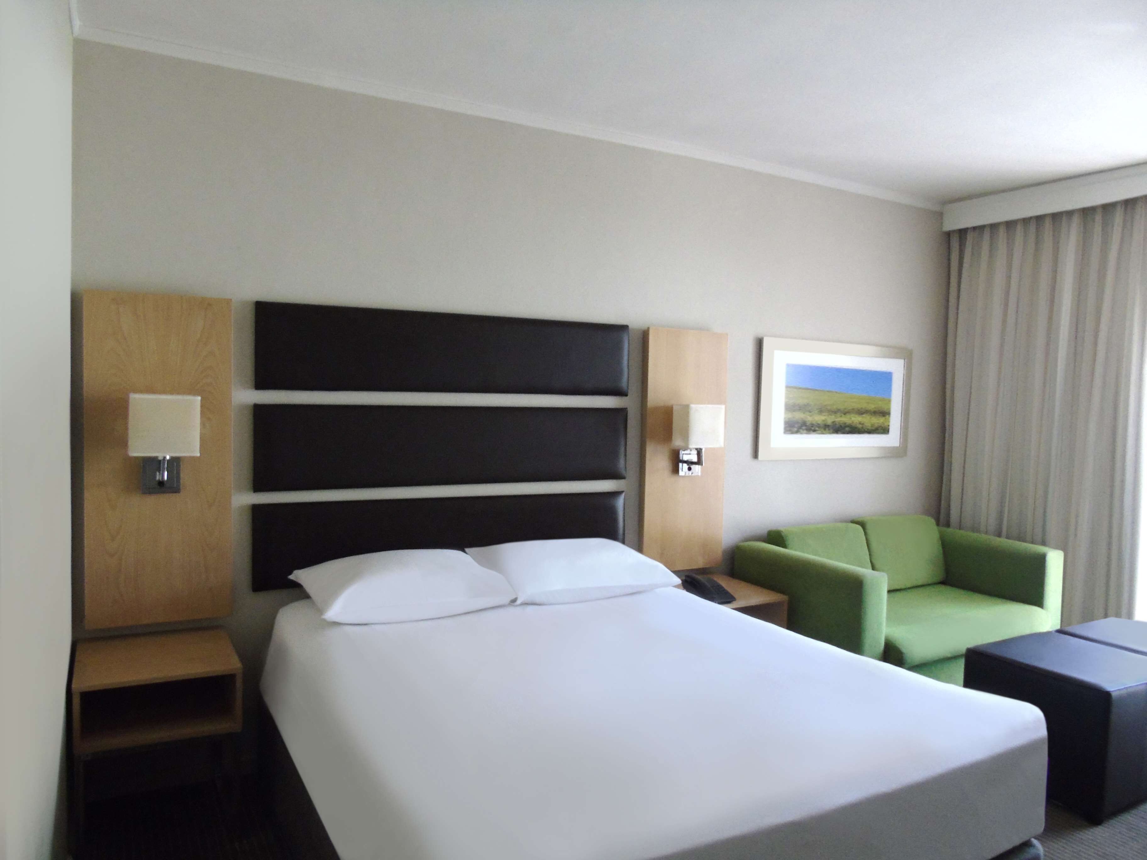 Et hotelværelse med en stor seng, en grøn lænestol, et lille bord og et natbord.