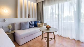 Una habitación de hotel moderna con un sofá, una mesa redonda de madera y un ventanal con cortinas translúcidas.