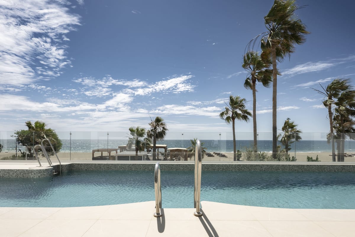 A swimming pool with a view of the beach and palm trees.
