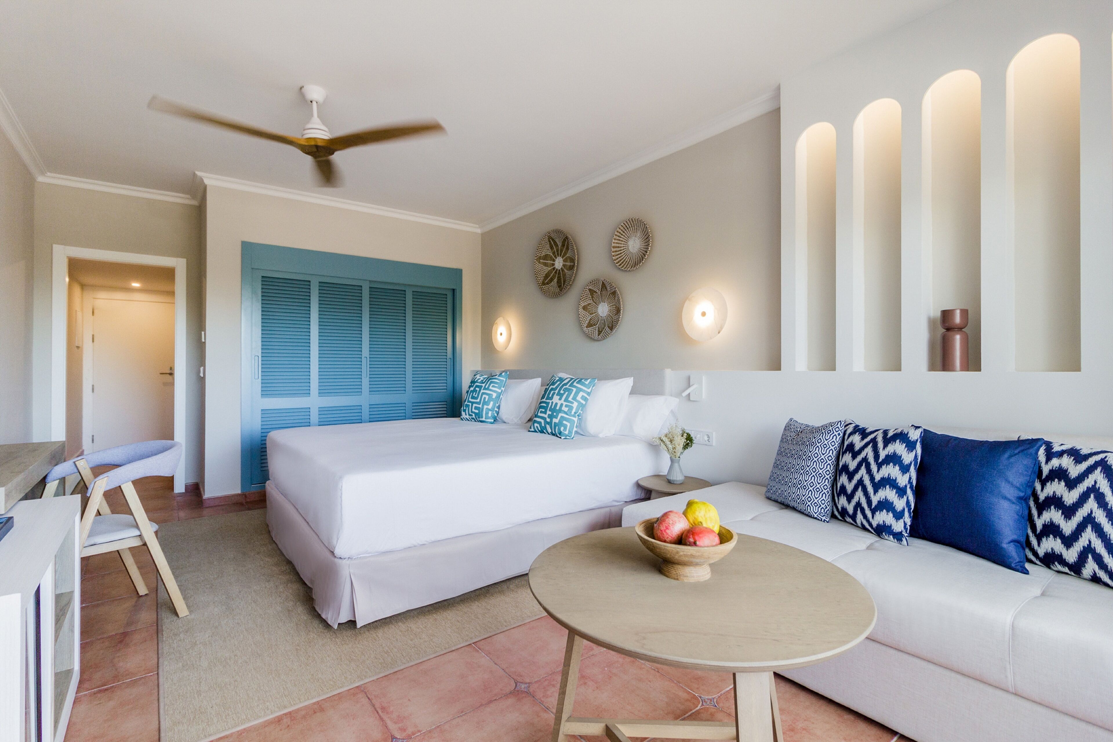 Una habitación de hotel moderna con cama, sofá, mesa de comedor y ventilador de techo.