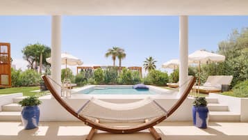 Una hamaca bajo un dosel blanco con vista a una piscina, rodeada de palmeras y sillas de descanso.