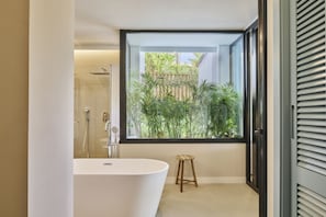 Ein modernes Badezimmer mit einer freistehenden Badewanne, einer Dusche und einem großen Fenster mit Blick auf Grünflächen.