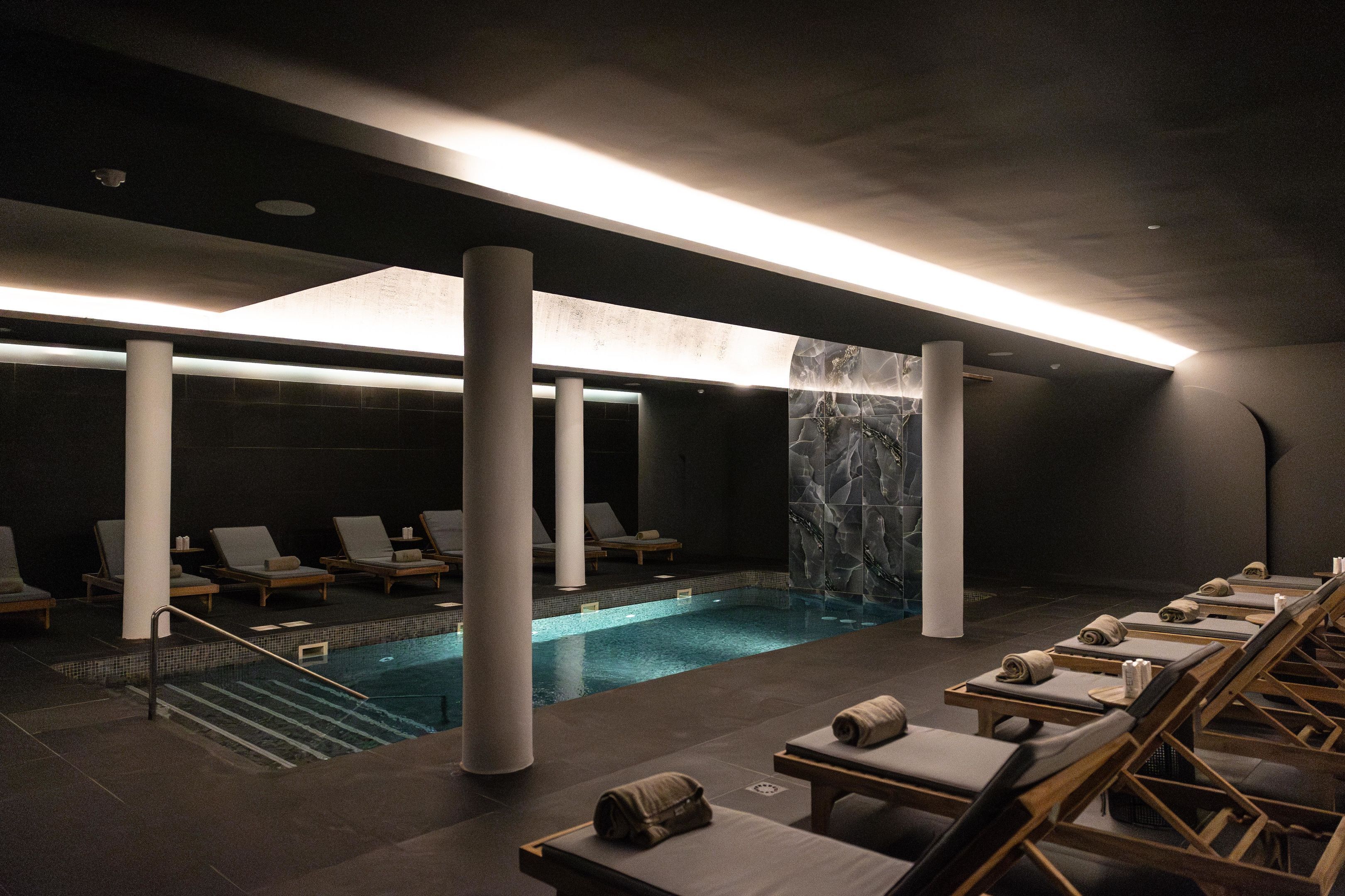 Un espace spa comprenant une piscine, des chaises longues et un mur en pierre.