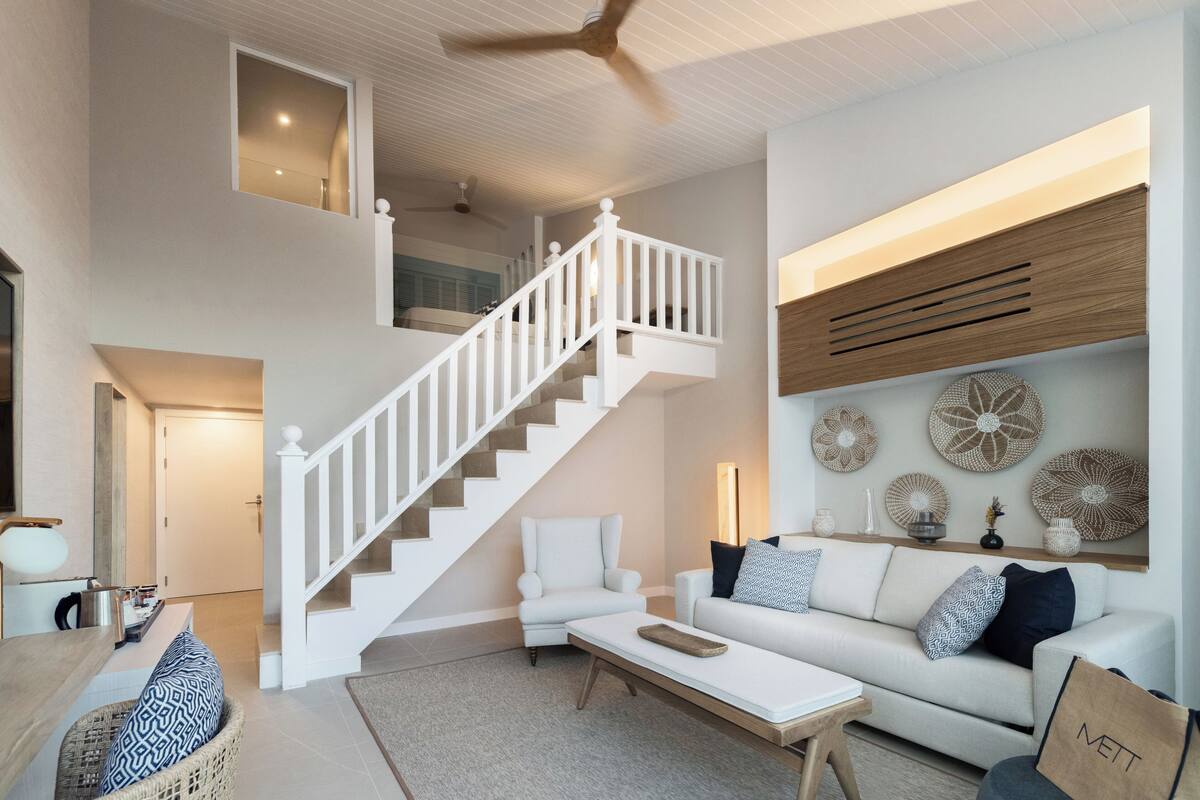 A spacious living area with a staircase, a white sofa, and decorative wall art.