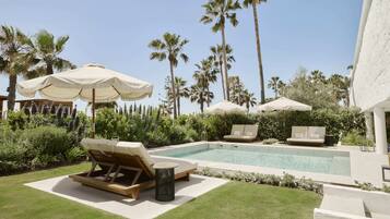 A pool area with lounge chairs and umbrellas, surrounded by palm trees and greenery.