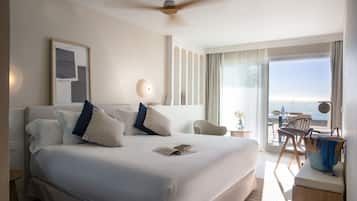 Habitación de hotel con una cama grande, ventilador de techo, escritorio con silla y vista al océano.