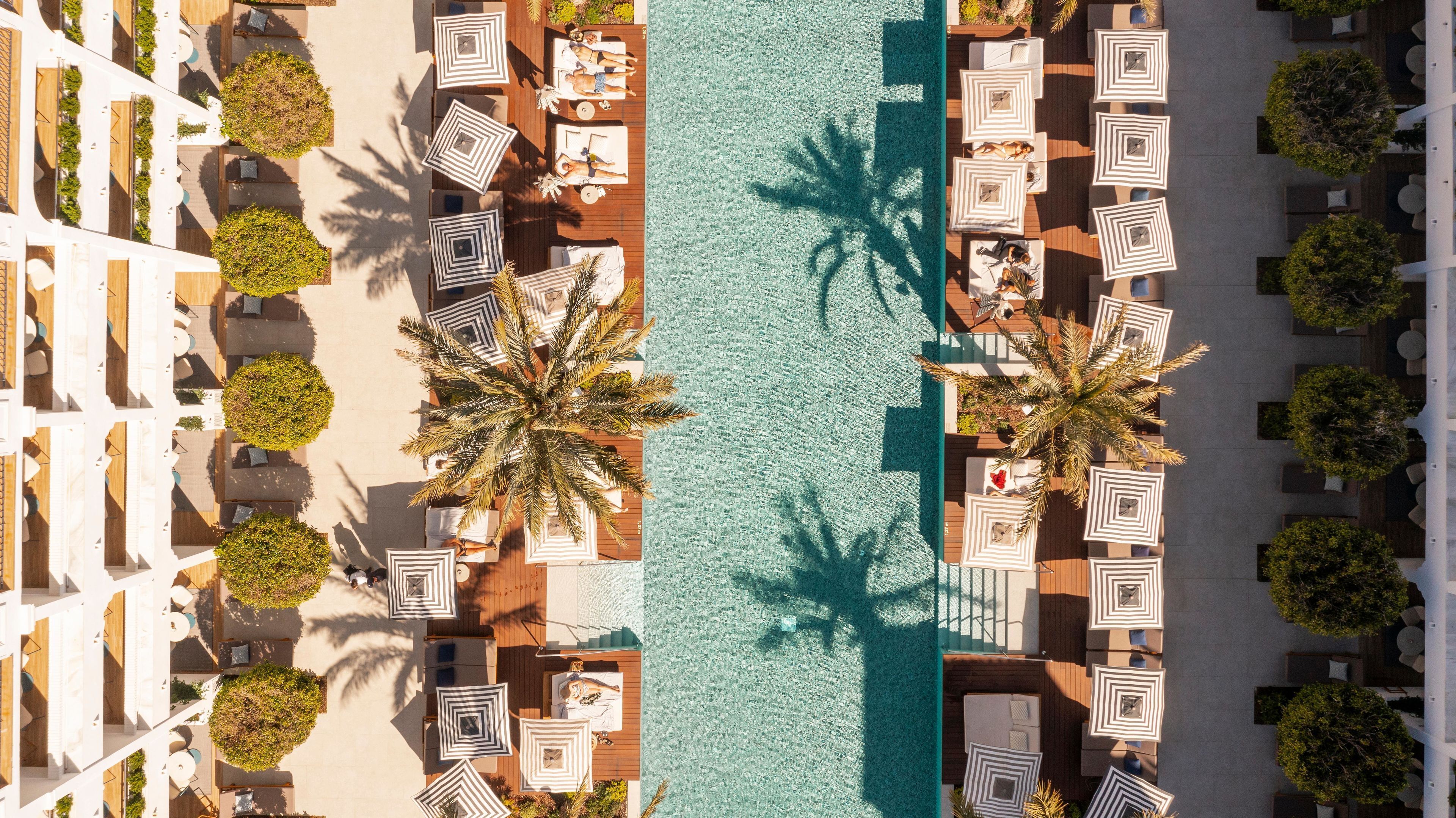 An aerial view of a resort with a pool, sun loungers, and palm trees.