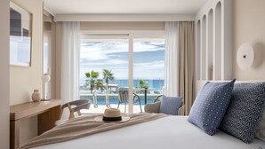 A hotel room with a bed, a desk, a chair, a table with chairs, and a view of the ocean.