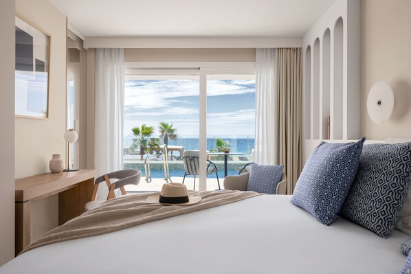 Una habitación de hotel con una cama, un escritorio, una silla, una mesa con sillas y vistas al océano.