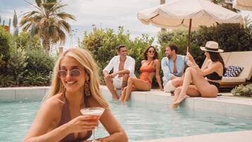 A poolside area with people relaxing and a woman holding a drink.