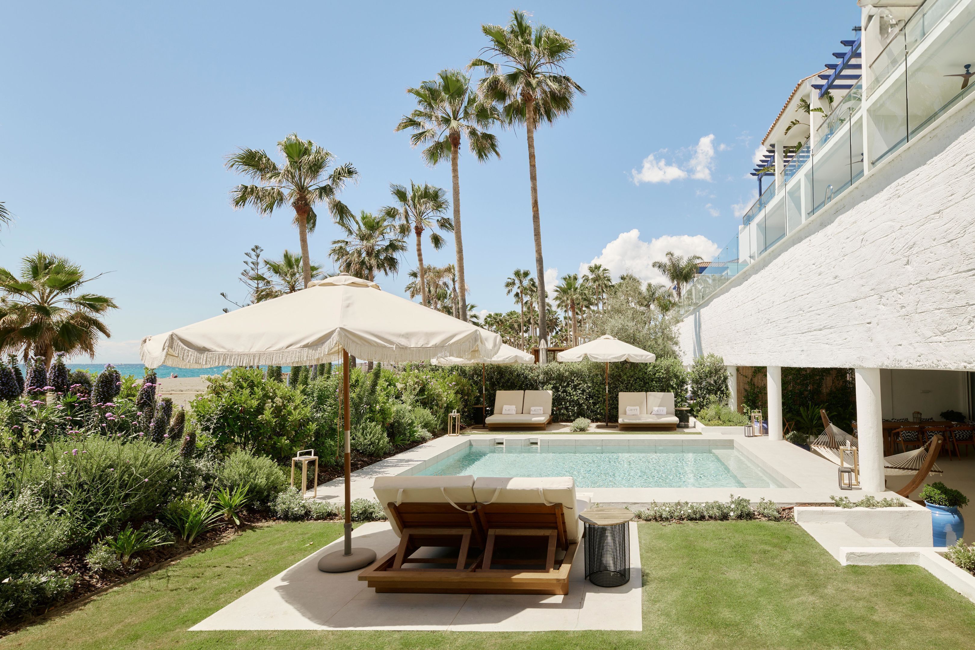 A pool area with lounge chairs, umbrellas, and palm trees.