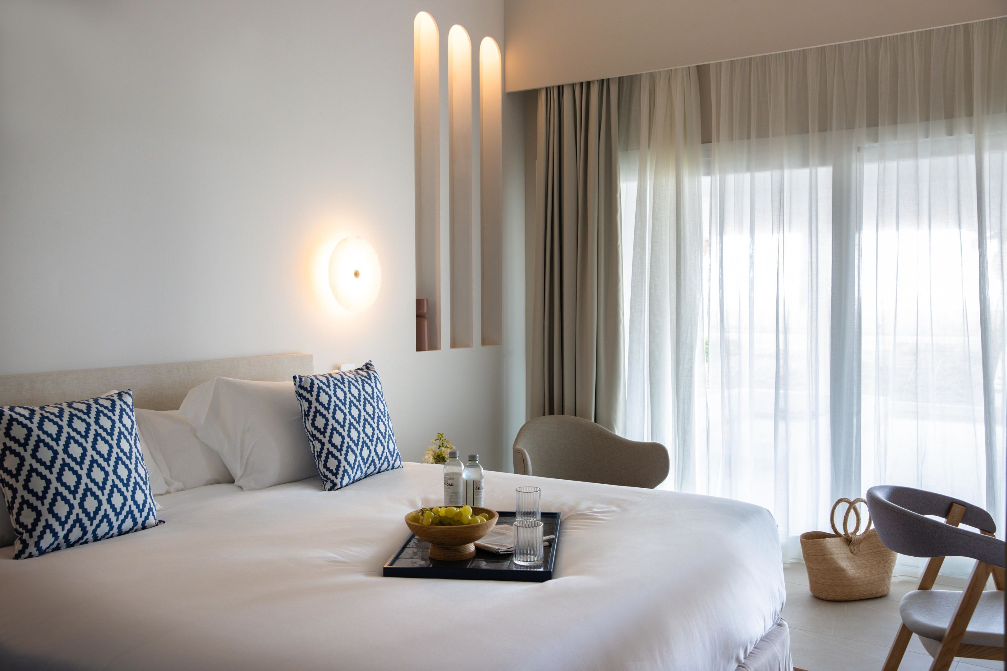 Una habitación de hotel con una cama grande, una mesita de noche con una bandeja, un cuenco de fruta y una silla.