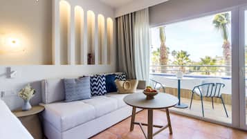 A modern hotel room with a sofa, a round table, and a balcony with a view of palm trees.