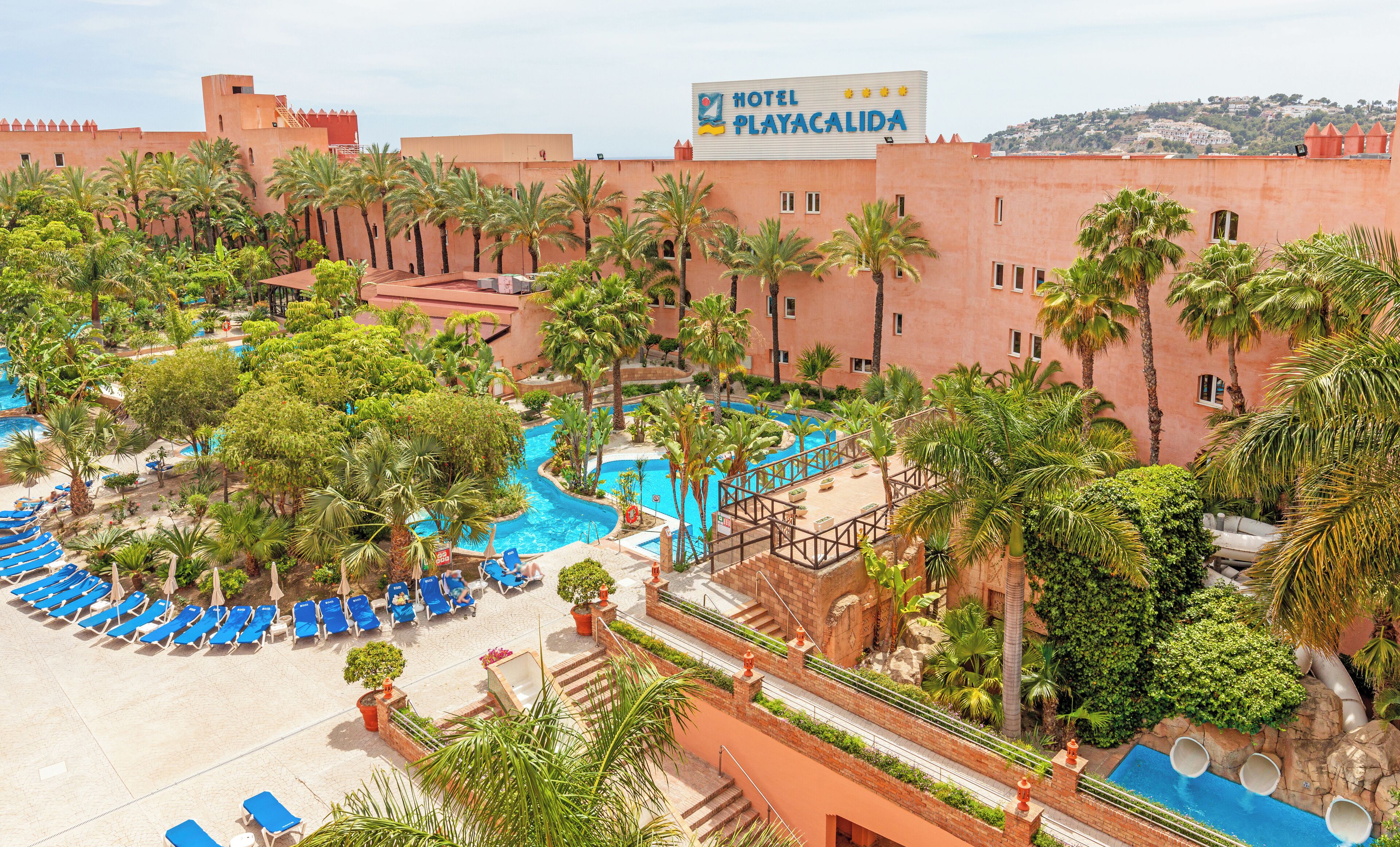 Un hotel con un amplio área de piscina, palmeras y un cartel que dice "HOTEL PLAYACALIDA".