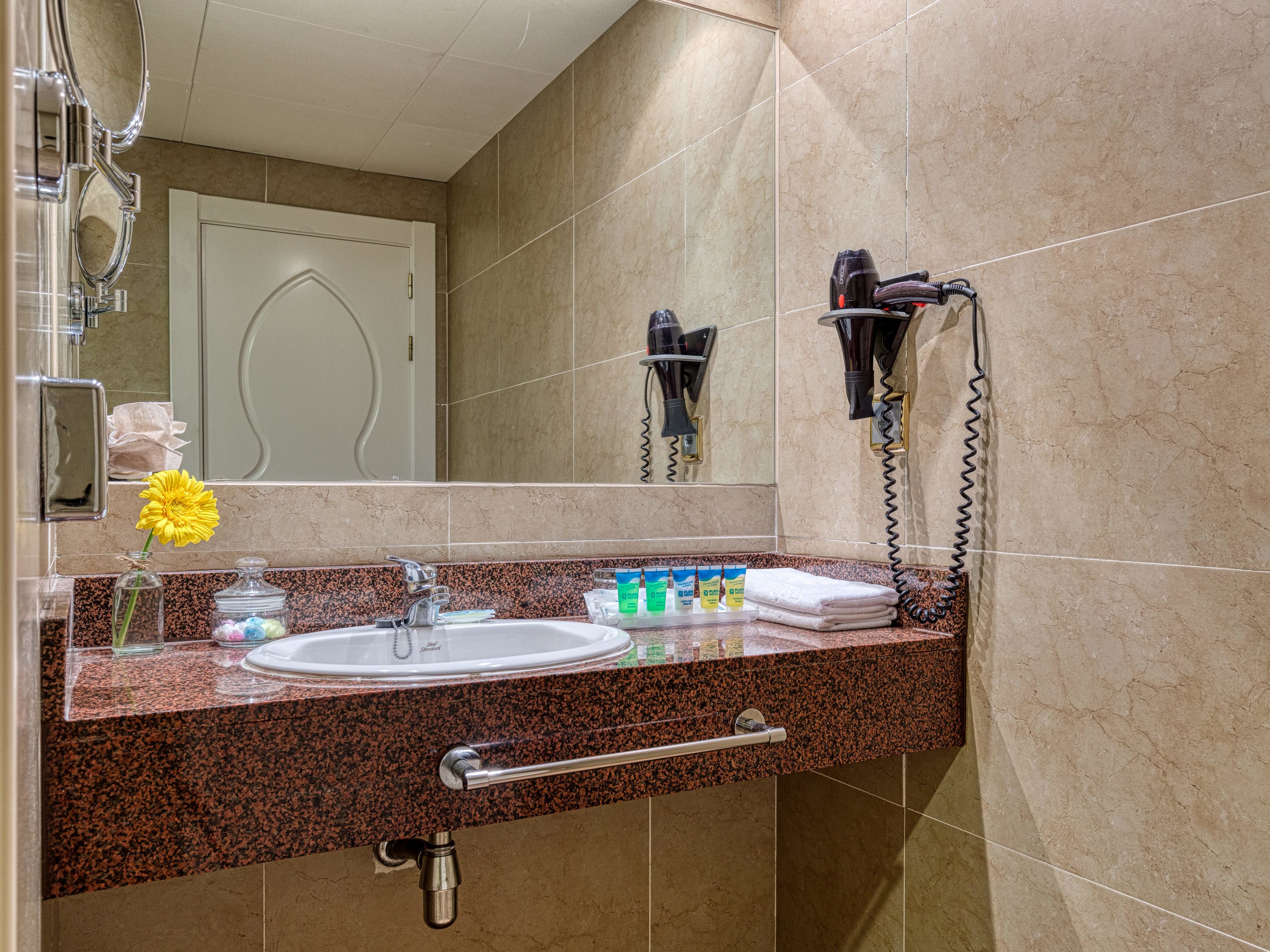 Une salle de bain équipée d’un lavabo, d’un miroir, d’un sèche-cheveux et d’un porte-serviettes.