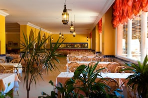 Enjoy meals in a warm and inviting dining area with tables set for guests, comfortable chairs, and a high ceiling with exposed beams.
