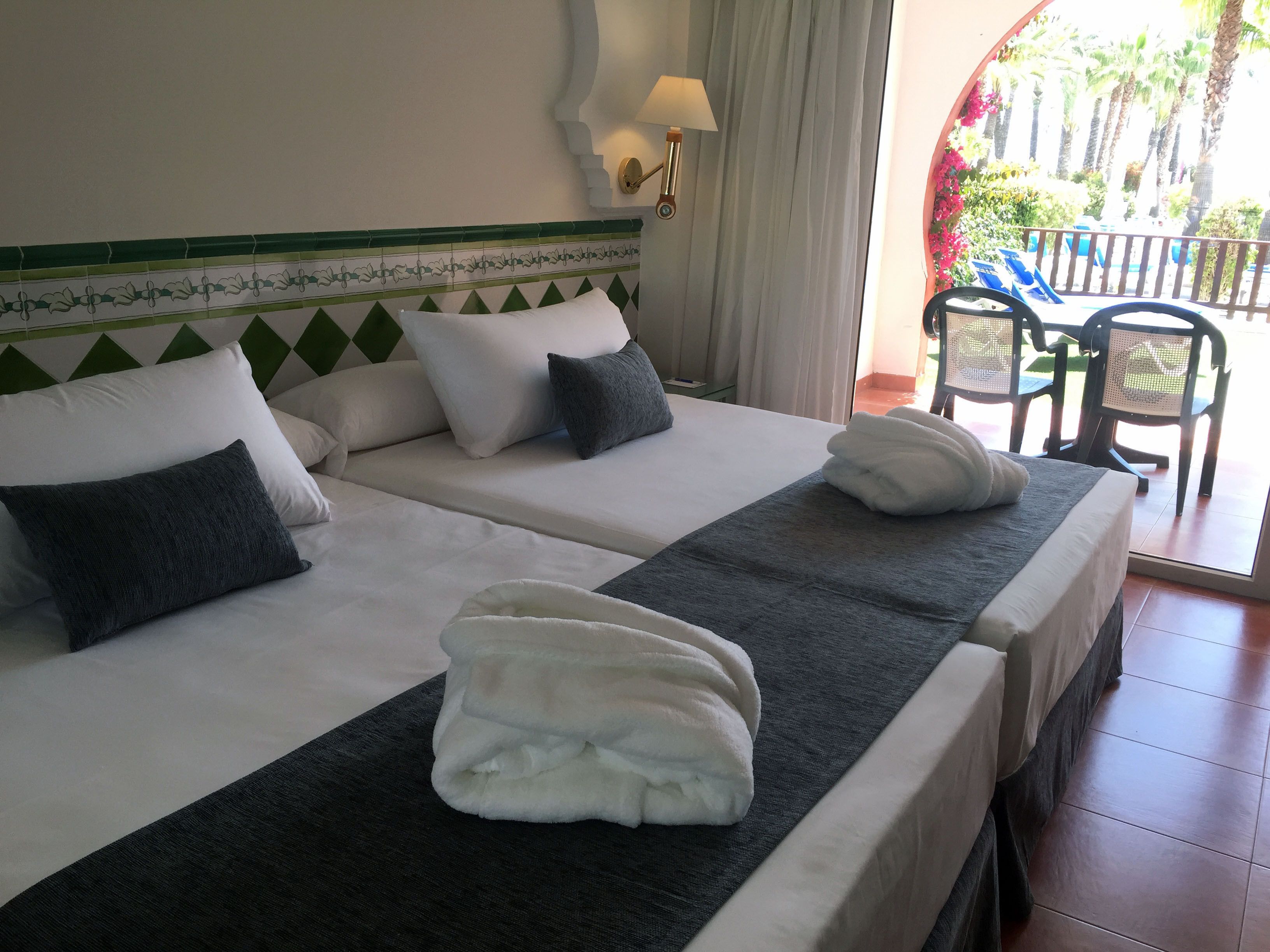 Habitación de hotel con dos camas, vista al exterior y una mesa con sillas.