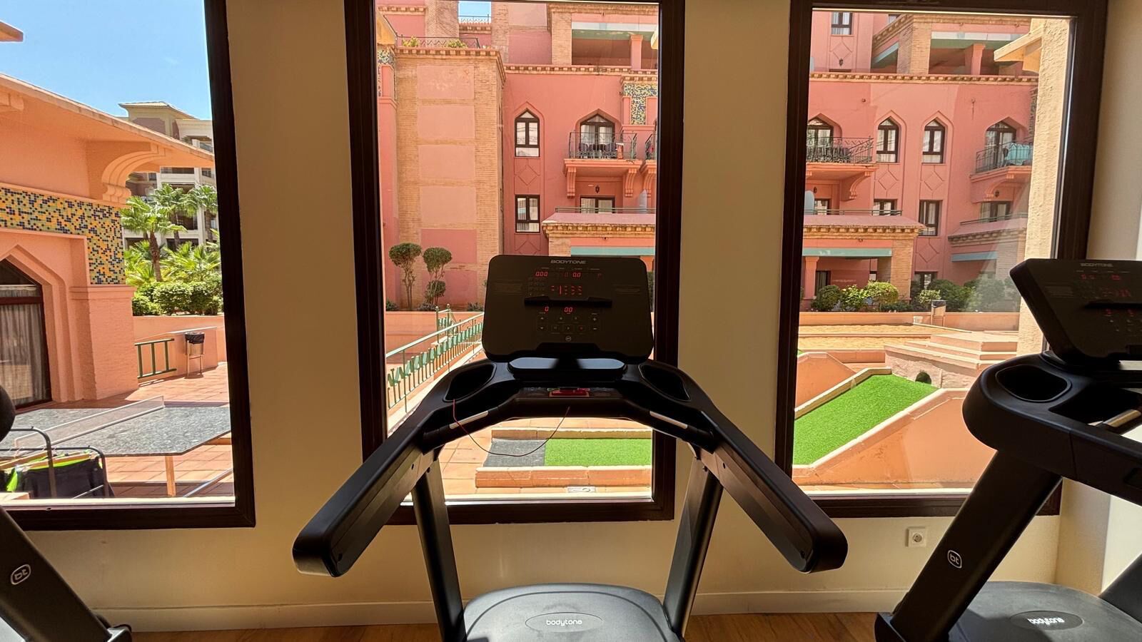 Una cinta de correr en una habitación con ventanas amplias que dan a un patio interior con un edificio al fondo.