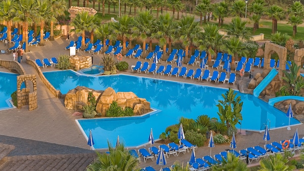 A resort pool area with multiple pools, lounge chairs, and palm trees. - Playacanela Hotel (Ayamonte)