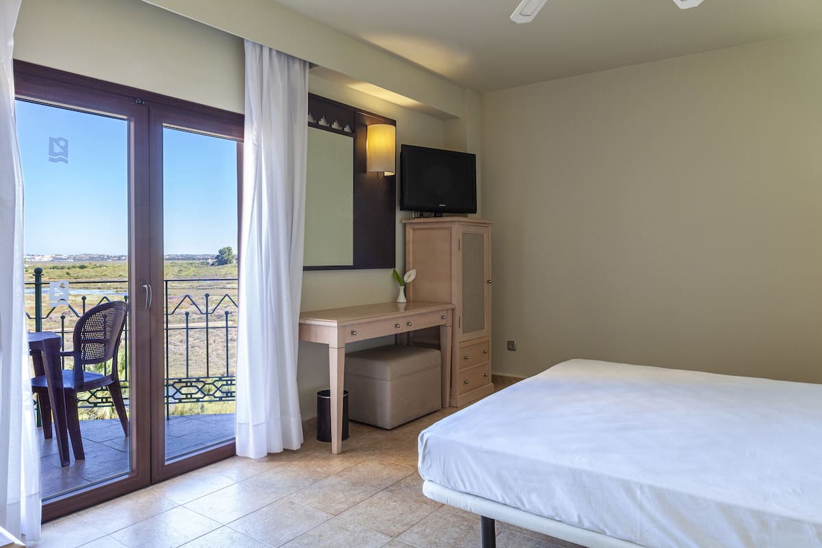 Une chambre d’hôtel comprenant un lit, un bureau avec une chaise, une télévision et un balcon donnant sur la campagne.