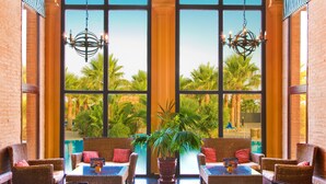 A room with large arched windows, wicker furniture, and a view of palm trees. - Playacanela Hotel (Ayamonte)