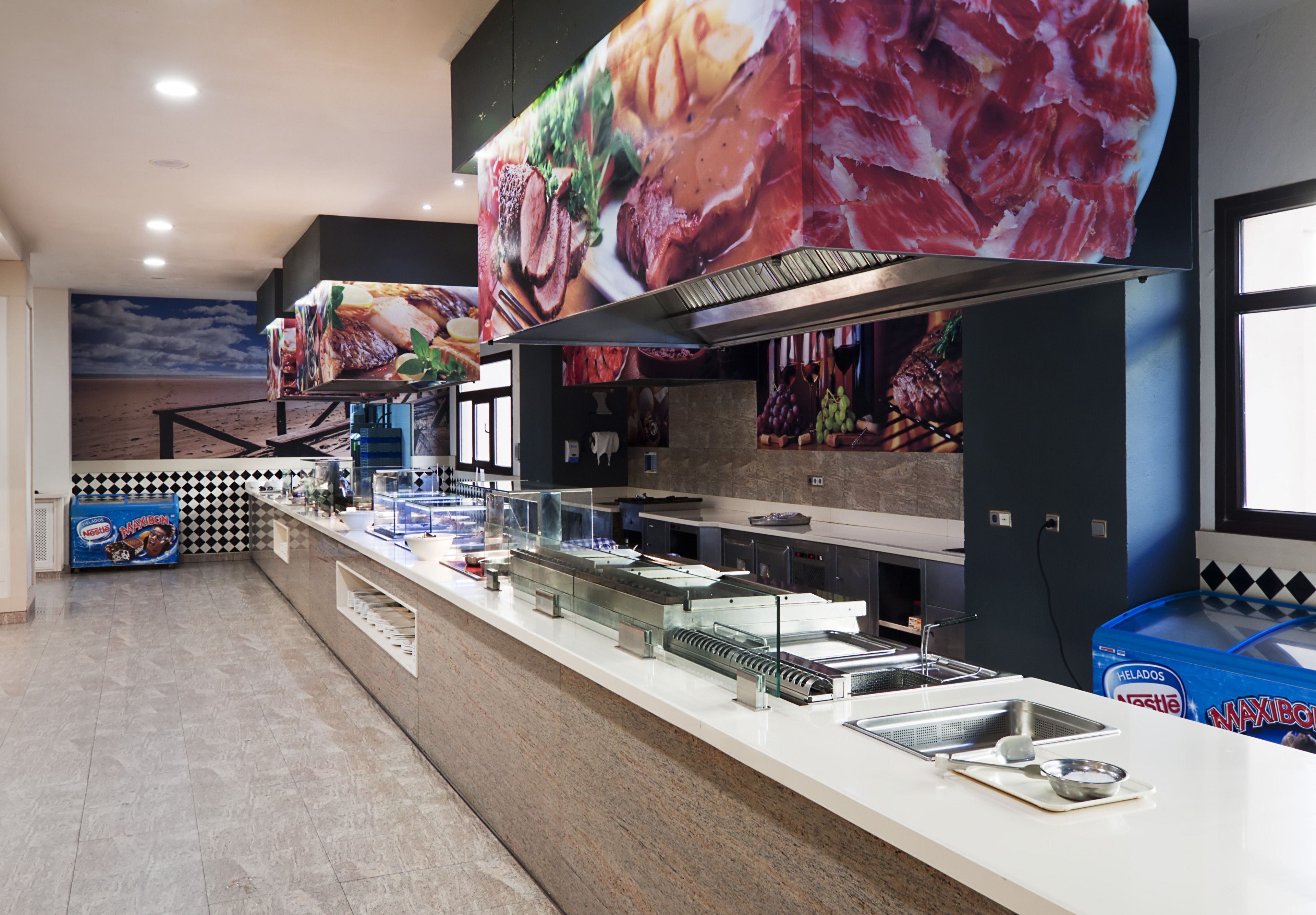 Zona de bufé con diversas mesas de comida, incluyendo carnes y verduras, y un mostrador con pileta y utensilios.