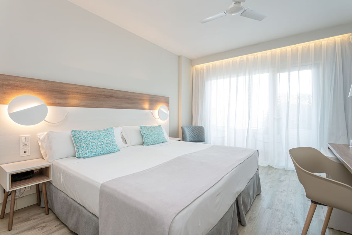 A modern hotel room with a large bed, bedside tables, a desk, and a chair.