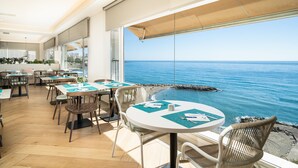 A restaurant with tables set for dining, overlooking a beach and the sea.