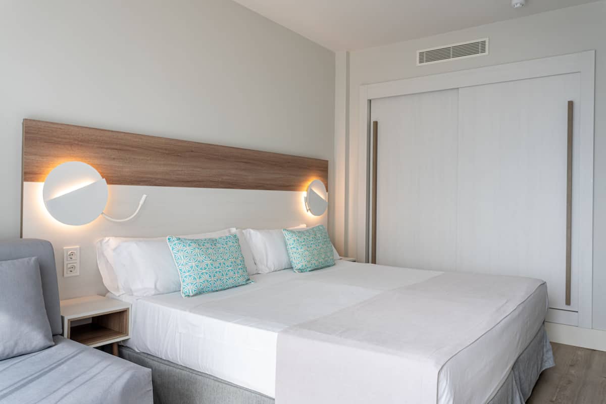 A modern hotel room with a large bed, two bedside tables, and a wardrobe.