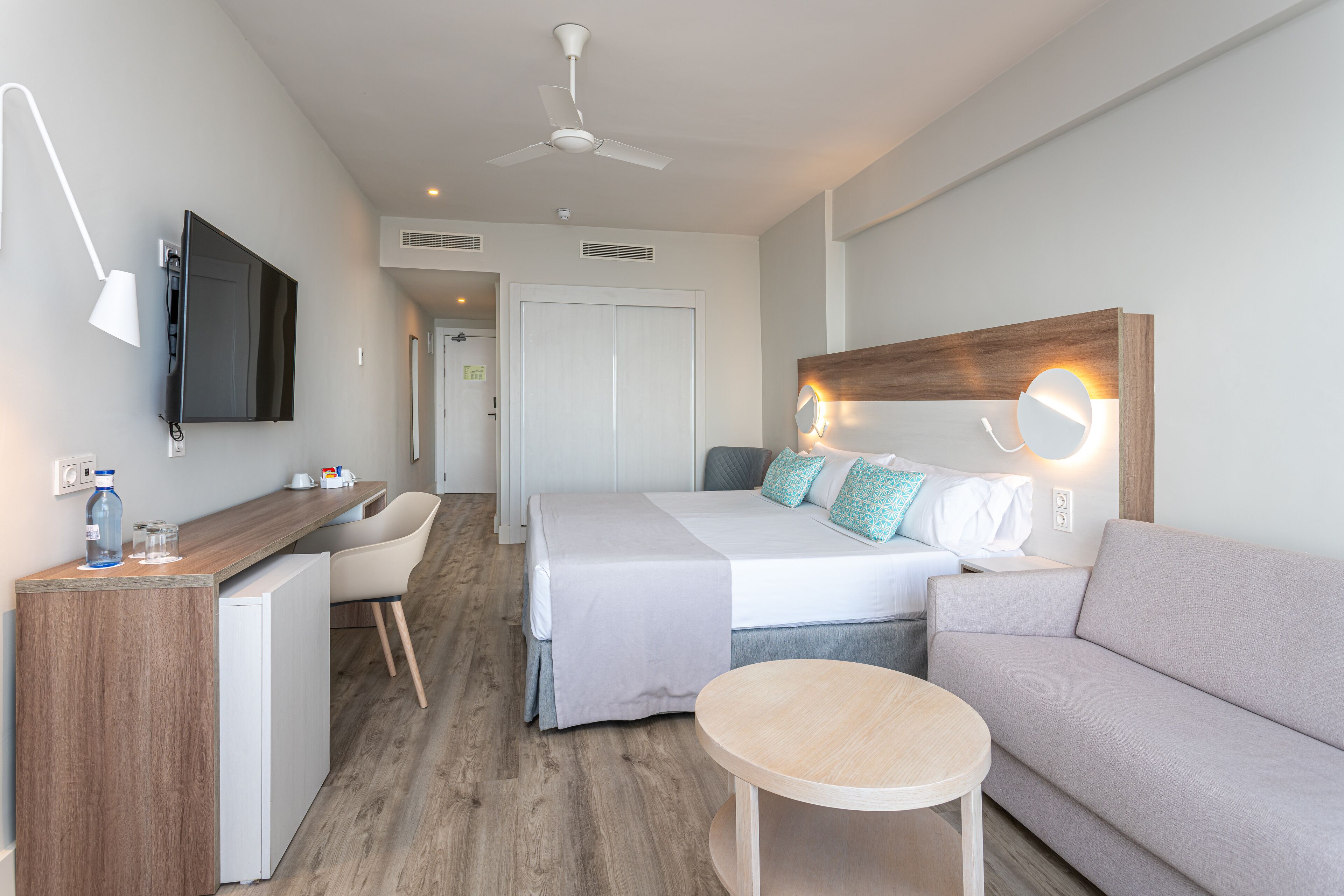 A modern hotel room with a bed, a sofa, a desk, and a small table.