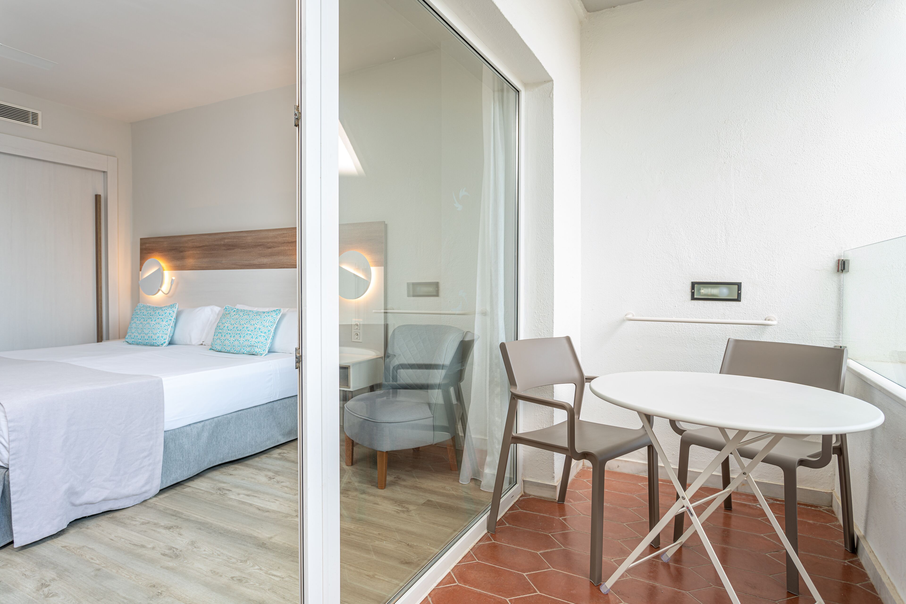 Una camera d'albergo con un letto, un piccolo tavolo con sedie e un divisorio in vetro.