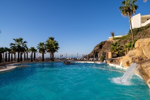 A swimming pool with clear blue water, surrounded by palm trees and a rocky hillside.