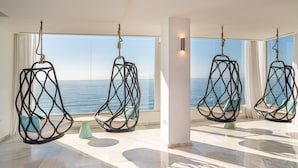 A spacious room with two hanging chairs facing a large window overlooking the sea.