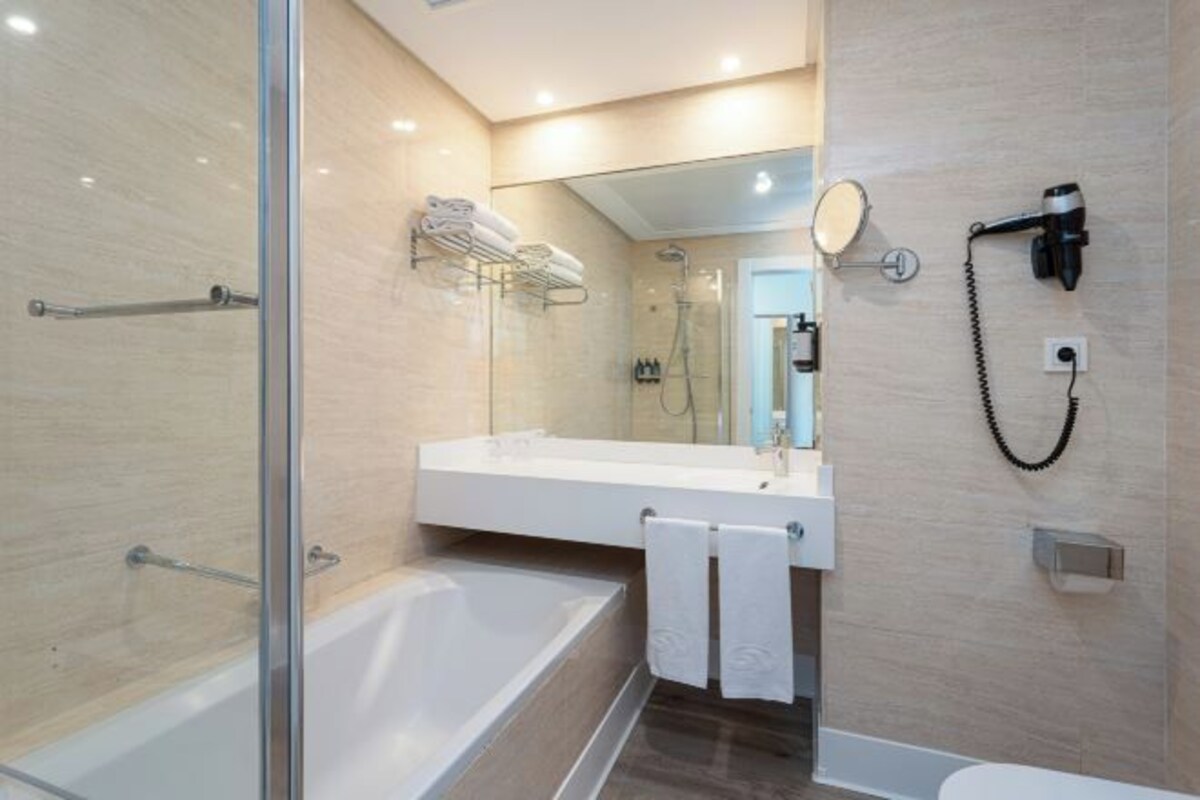 Un baño moderno con ducha de vidrio, bañera independiente y tocador con espejo y toallero.